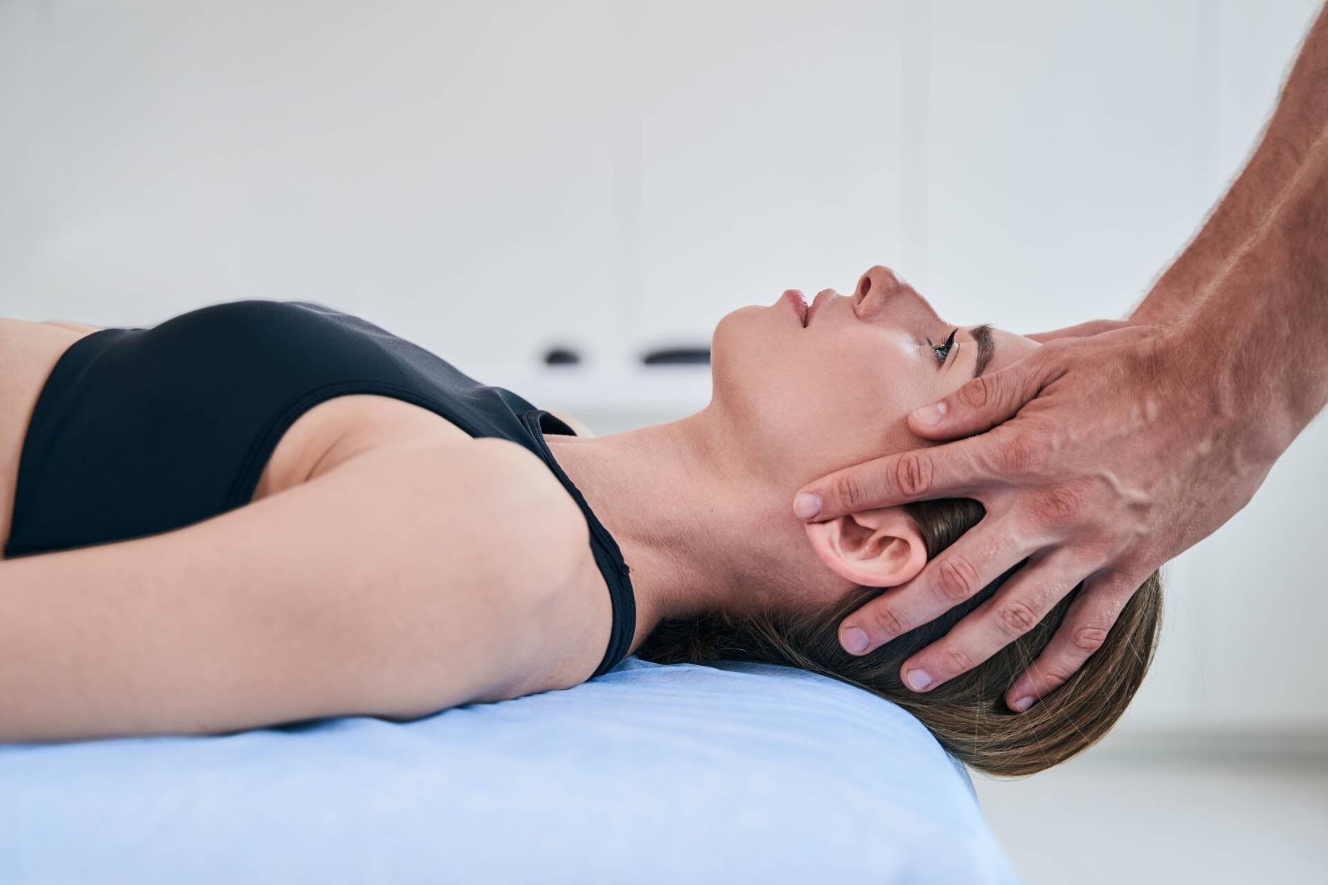 Close up side view portrait of beautiful elegant female lying on medical couch while man hands holding her head in medical office