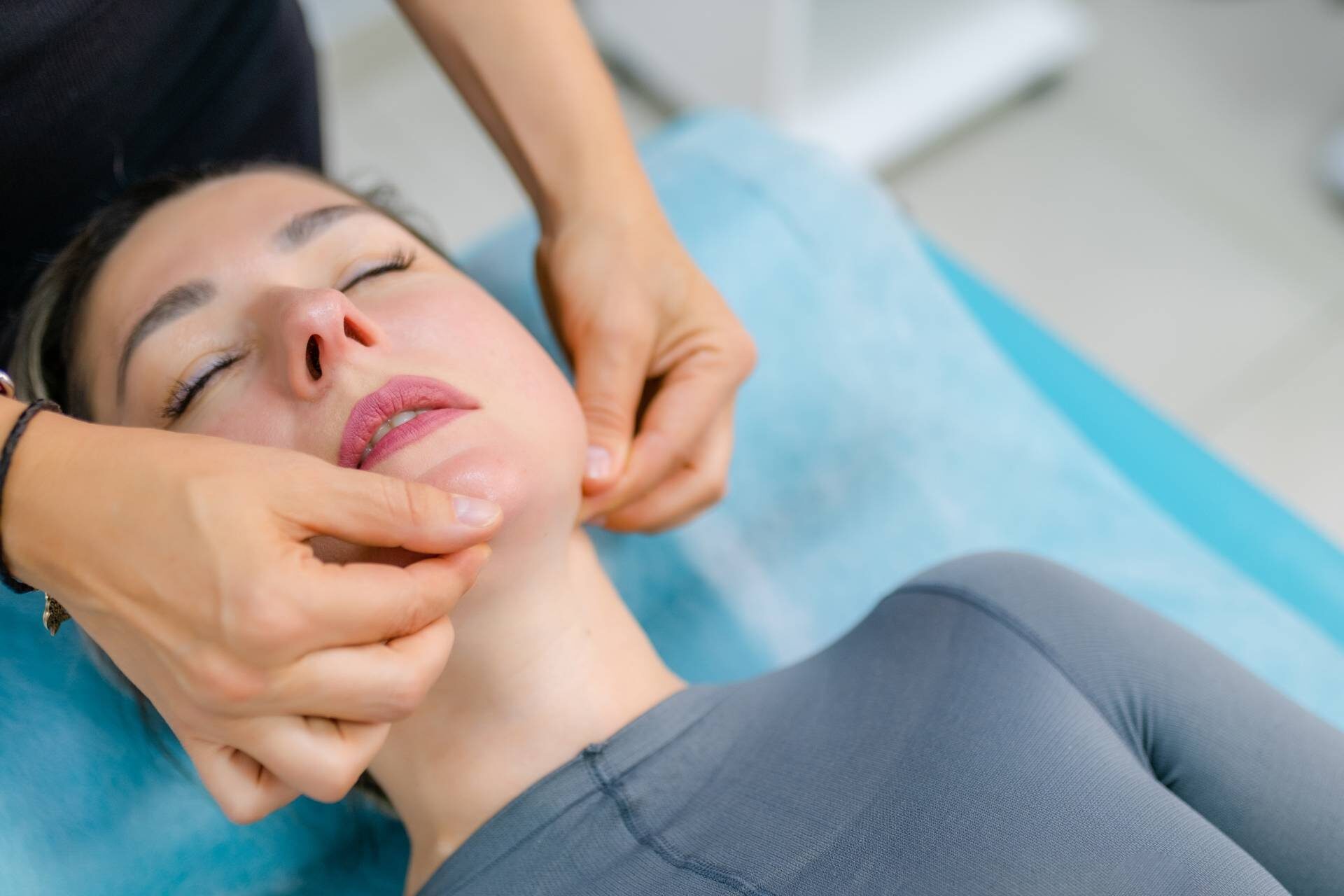 Close-up hands of an unidentified young woman masseur doing facial massage to beautiful young caucasian client woman at spa salon. Concept of therapeutic anti-aging skin tightening facial treatments.